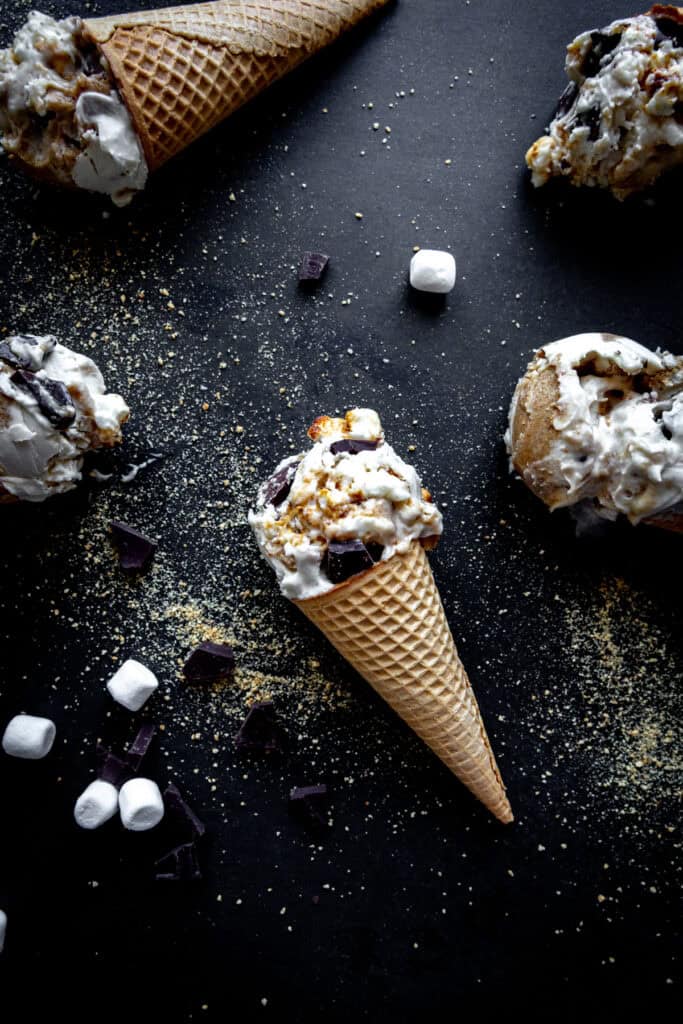 S'mores ice cream cones laying on a black background with marshmallows and chocolate chunks.