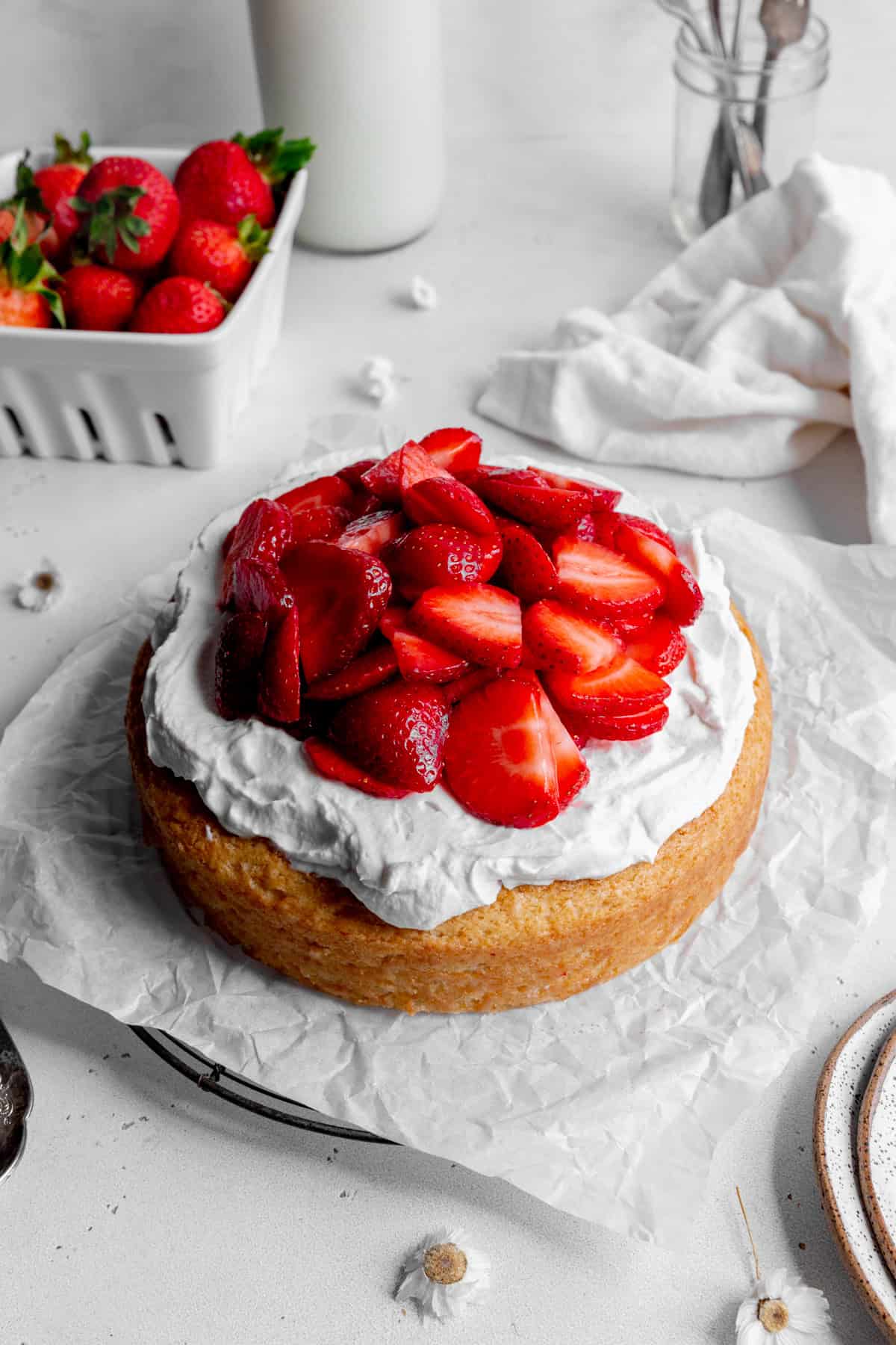 Strawberry shortcake cake on a wire rack and a basket of strawberries.