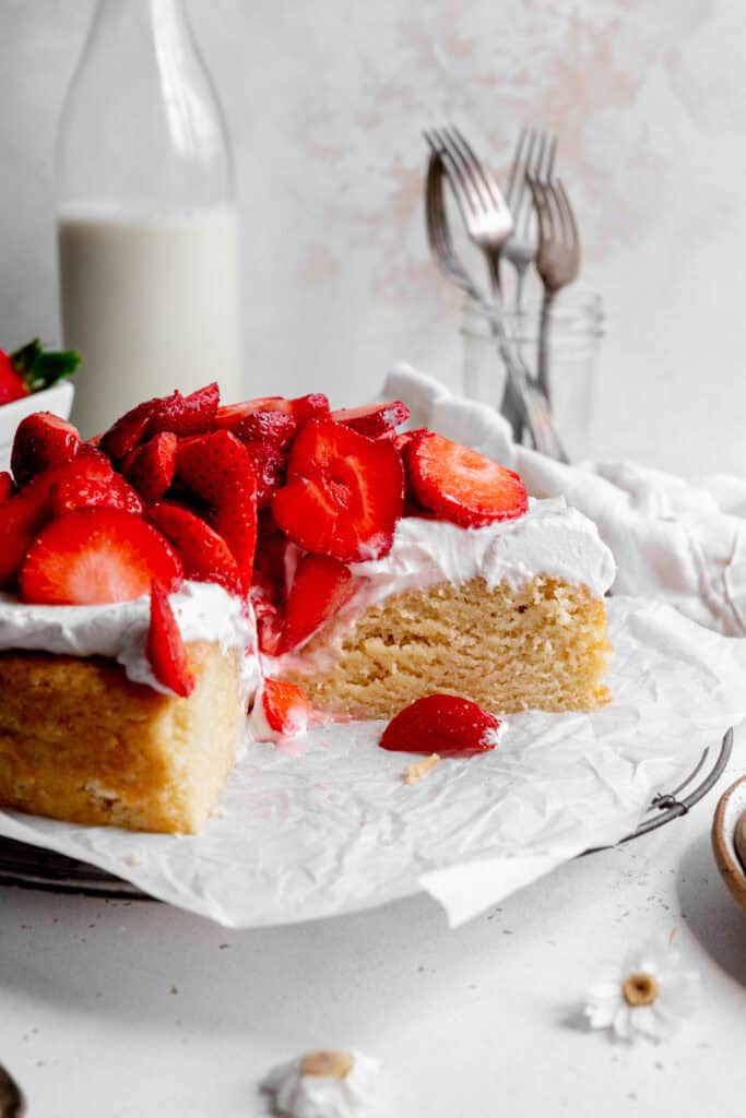 Shortcake topped with whipped cream and strawberries with slices missing.