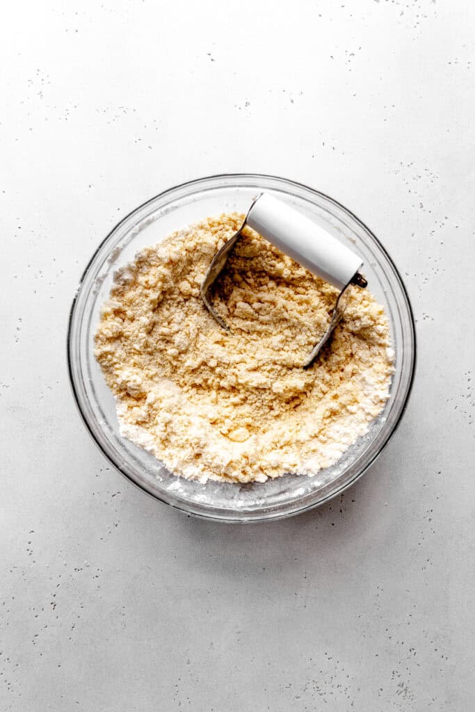 Pastry cutter in a glass bowl with flour, sugar and butter.