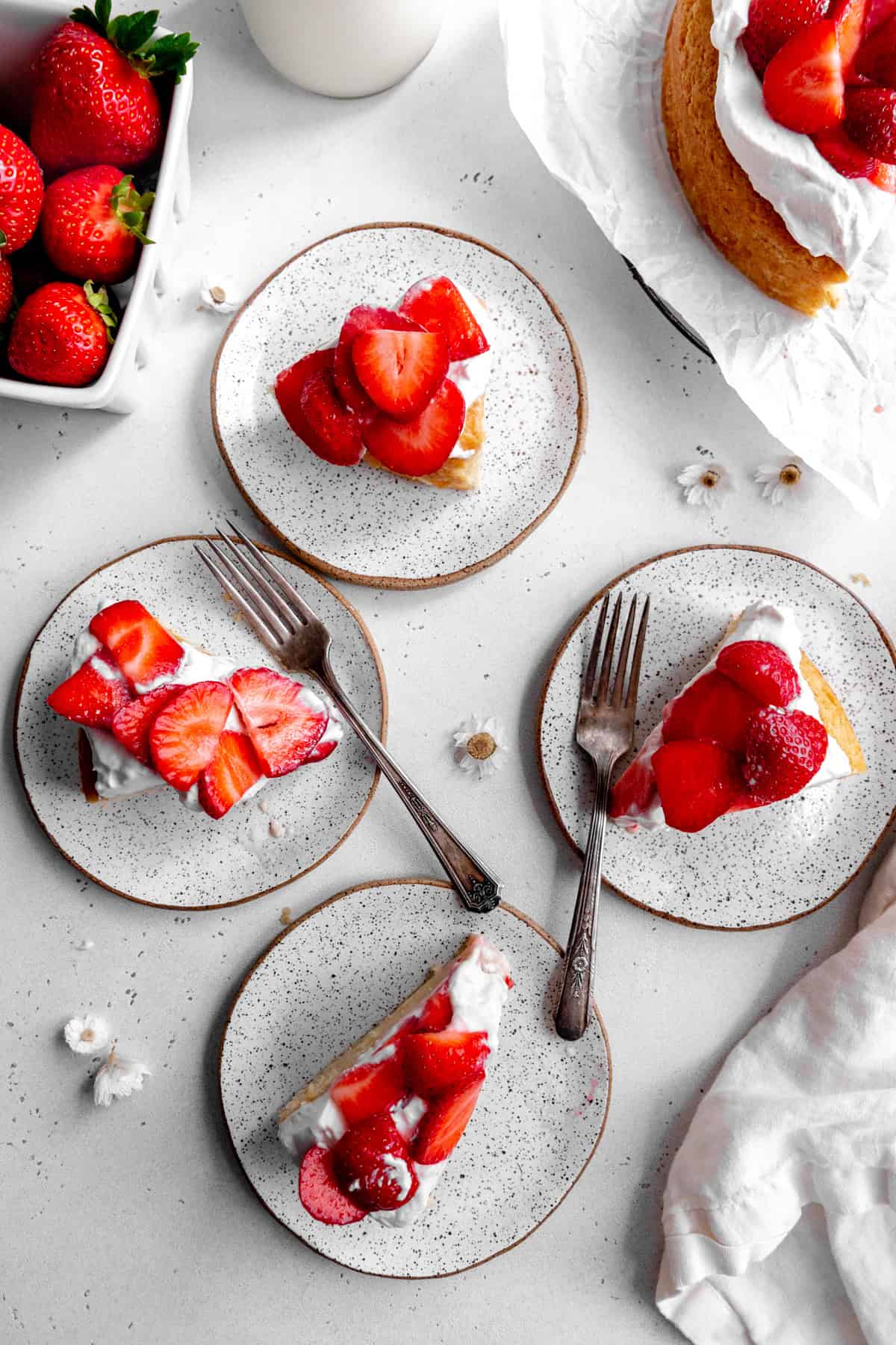 Slices of strawberry shortcake cake on plates and a jug of milk.