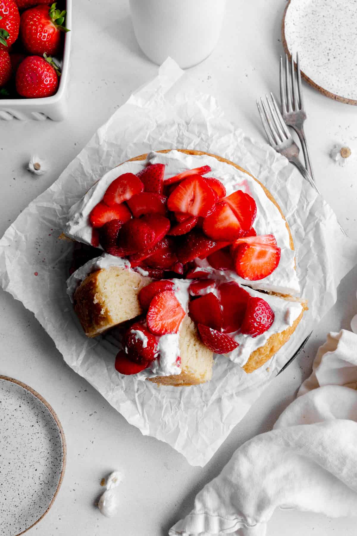 Strawberry shortcake cake, forks, a linen napkin and a jug of milk.