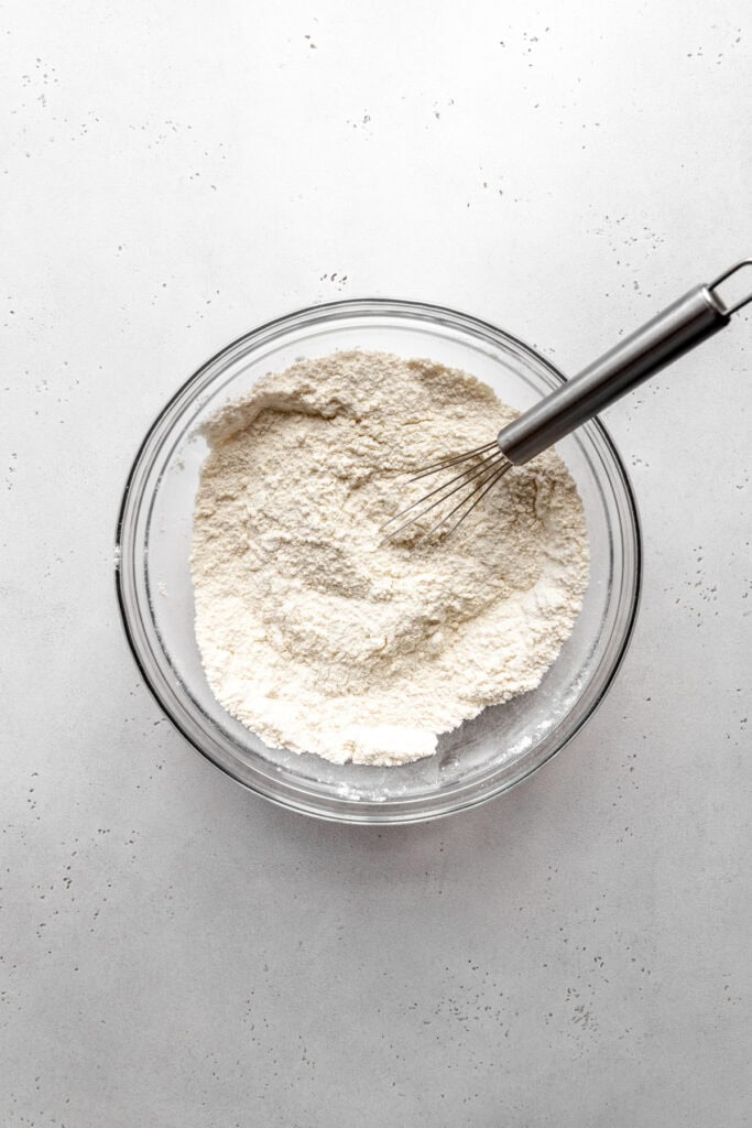 Flour in a glass bowl with a wire whisk.