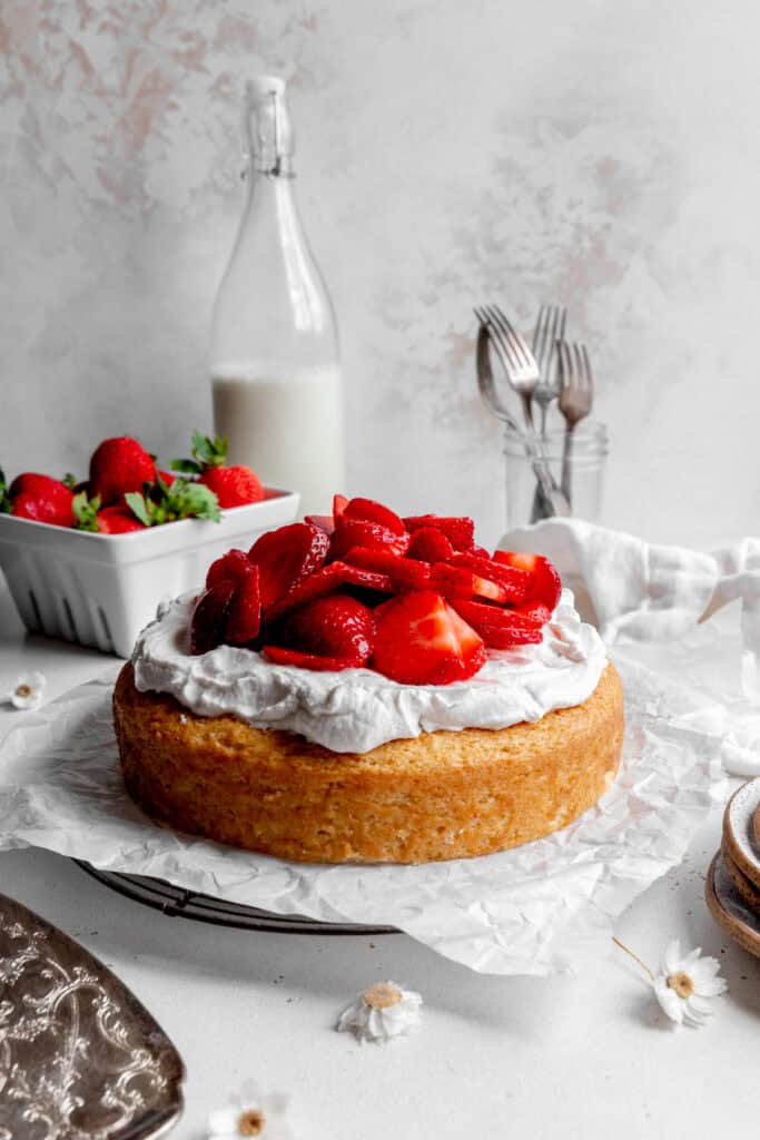 Strawberry shortcake cake, a cup of forks, a jug of milk and a basket of strawberries.