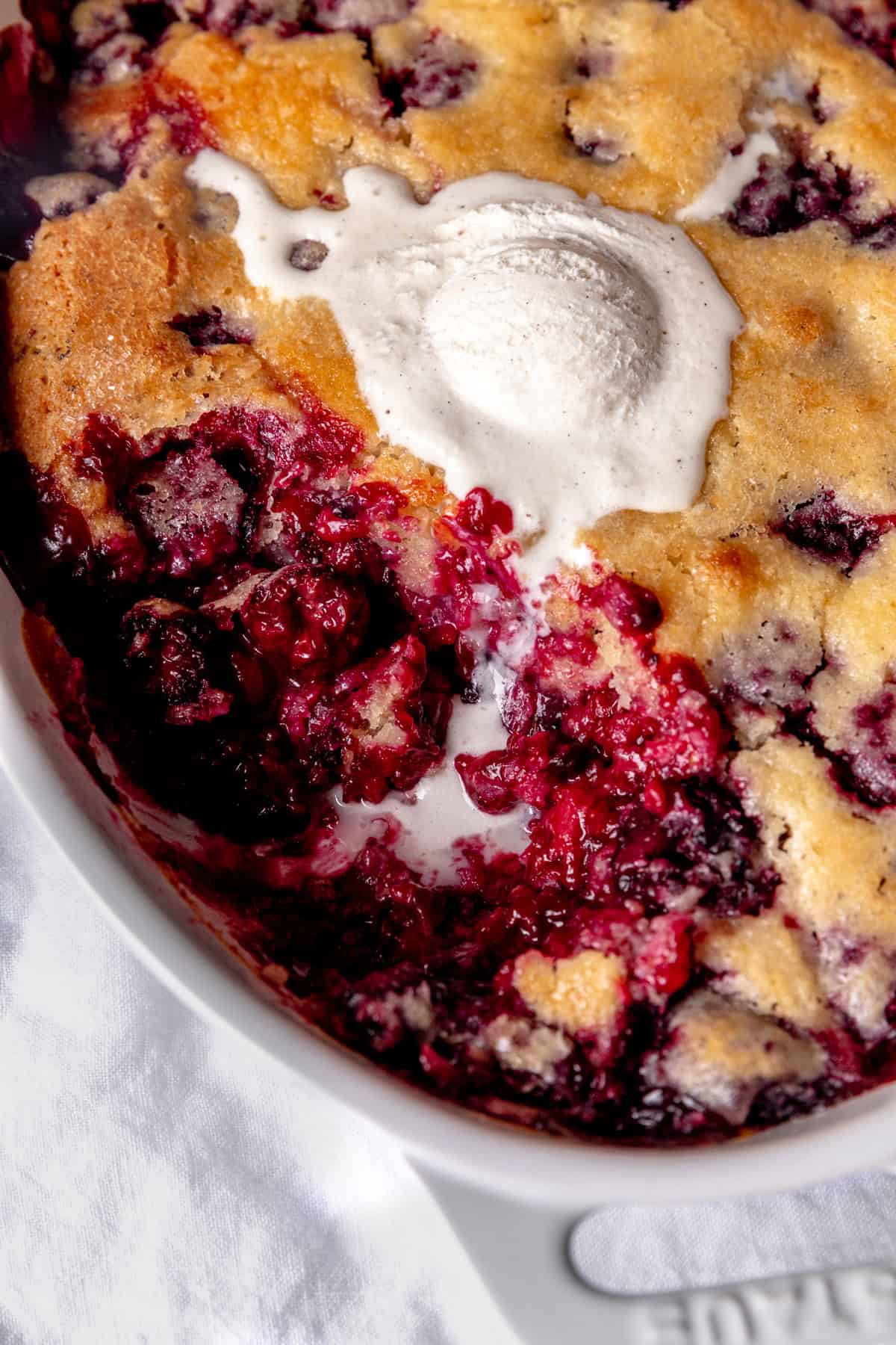 Blackberry cobbler in a white dish, covered in melted vanilla ice cream.