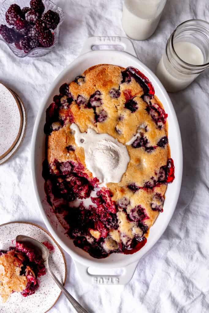 Blackberry cobbler topped with melted ice cream, a glass of milk and some cobbler on a plate.