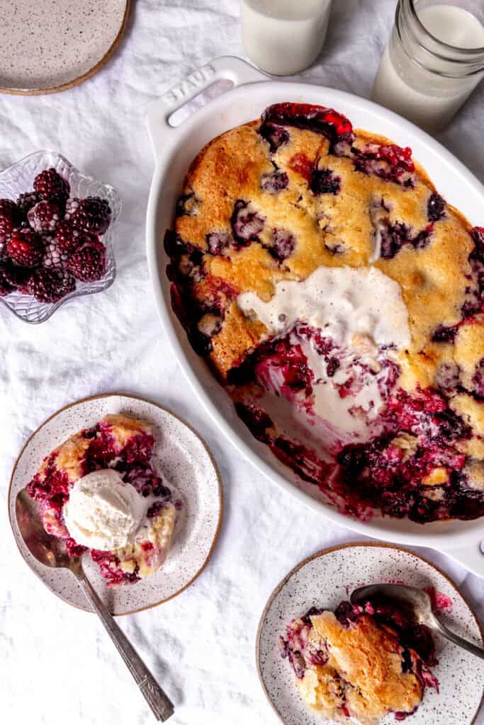 Dish of blackberry cobbler, blackberry cobbler on plates and a glass of milk.