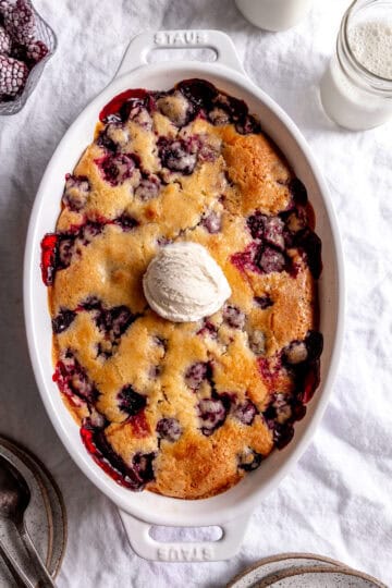 Blackberry cobbler, a bowl of blackberries, a glass of milk and some plates.