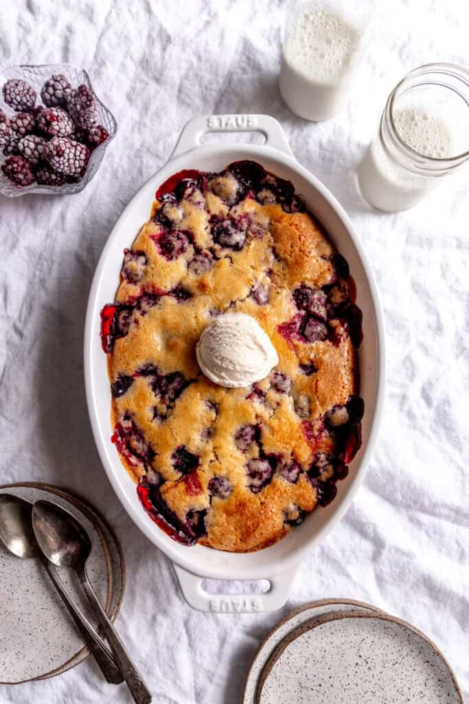 Blackberry cobbler, a bowl of blackberries, a glass of milk and some plates.