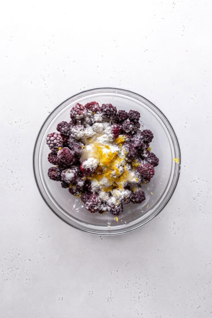 Glass bowl of blackberries covered in flour, sugar and lemon zest.