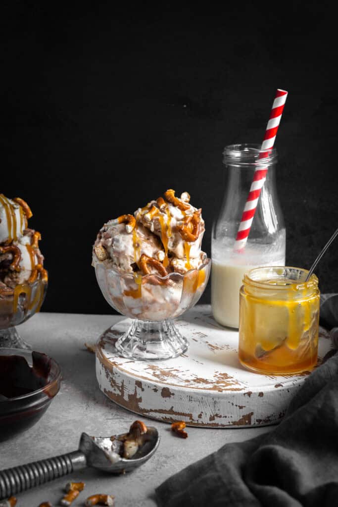 Dish of caramel pretzel ice cream, a jug of milk and a jar of caramel sauce with a spoon.