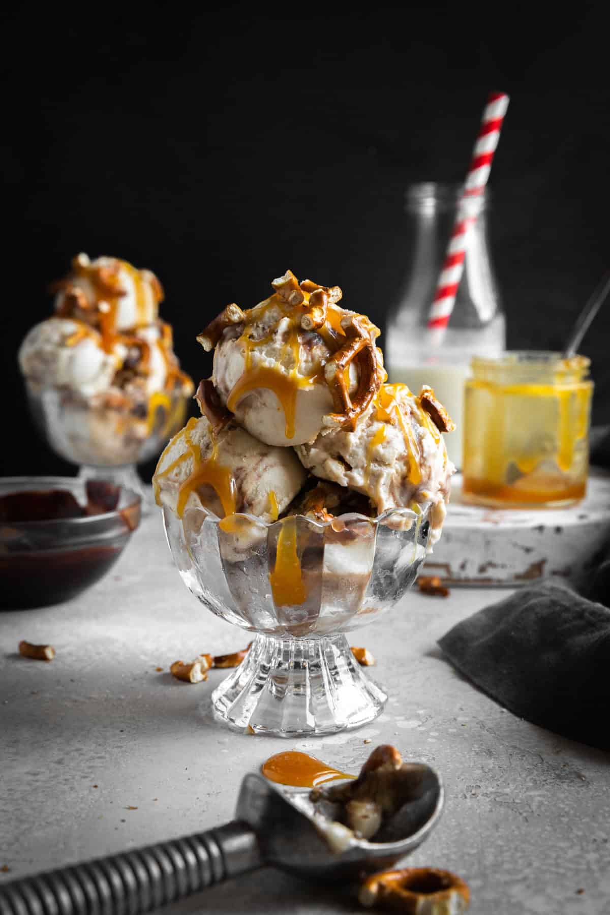 Scoops of caramel pretzel ice cream in a glass dish and an ice cream scoop.