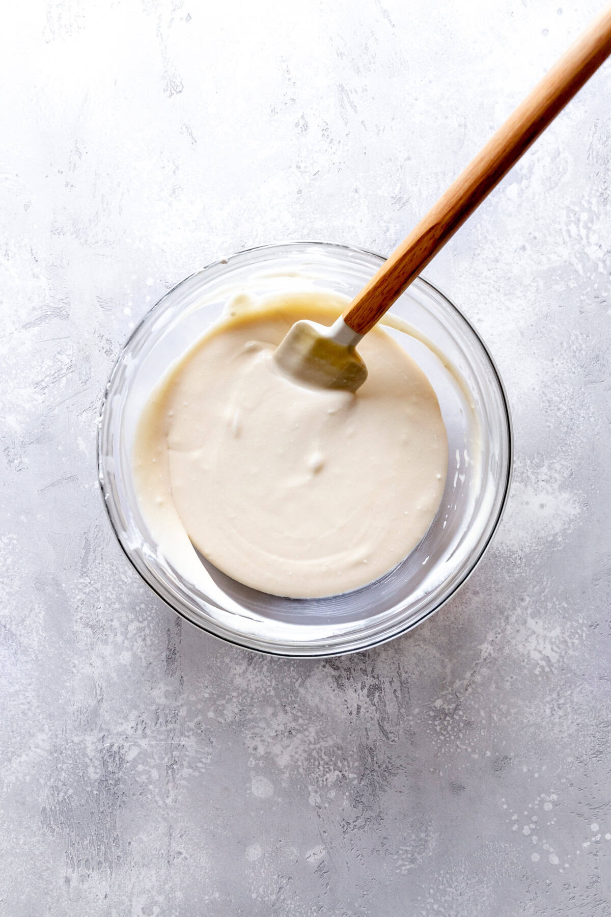 Glass bowl of vanilla ice cream base and a rubber spatula.