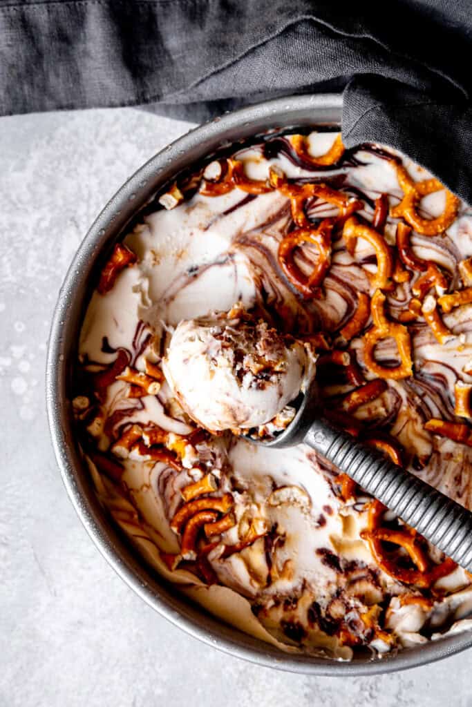 Ice cream scoop digging into a pan of caramel pretzel ice cream.