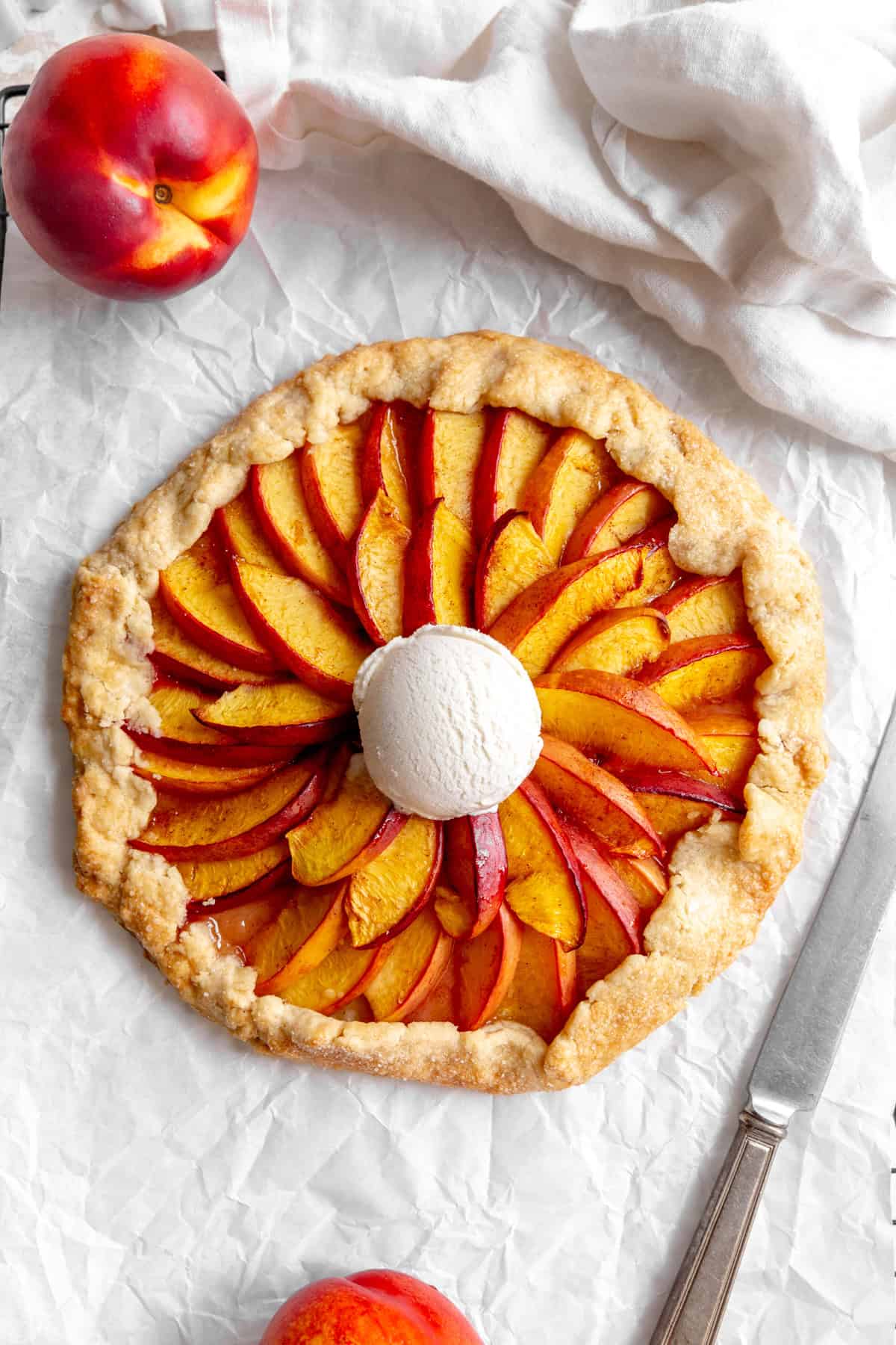 Nectarine galette topped with ice cream, fresh nectarines and a knife.