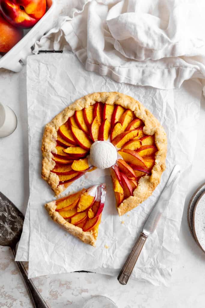Sliced nectarine galette on a wire rack, a stack of plates and a glass of milk.