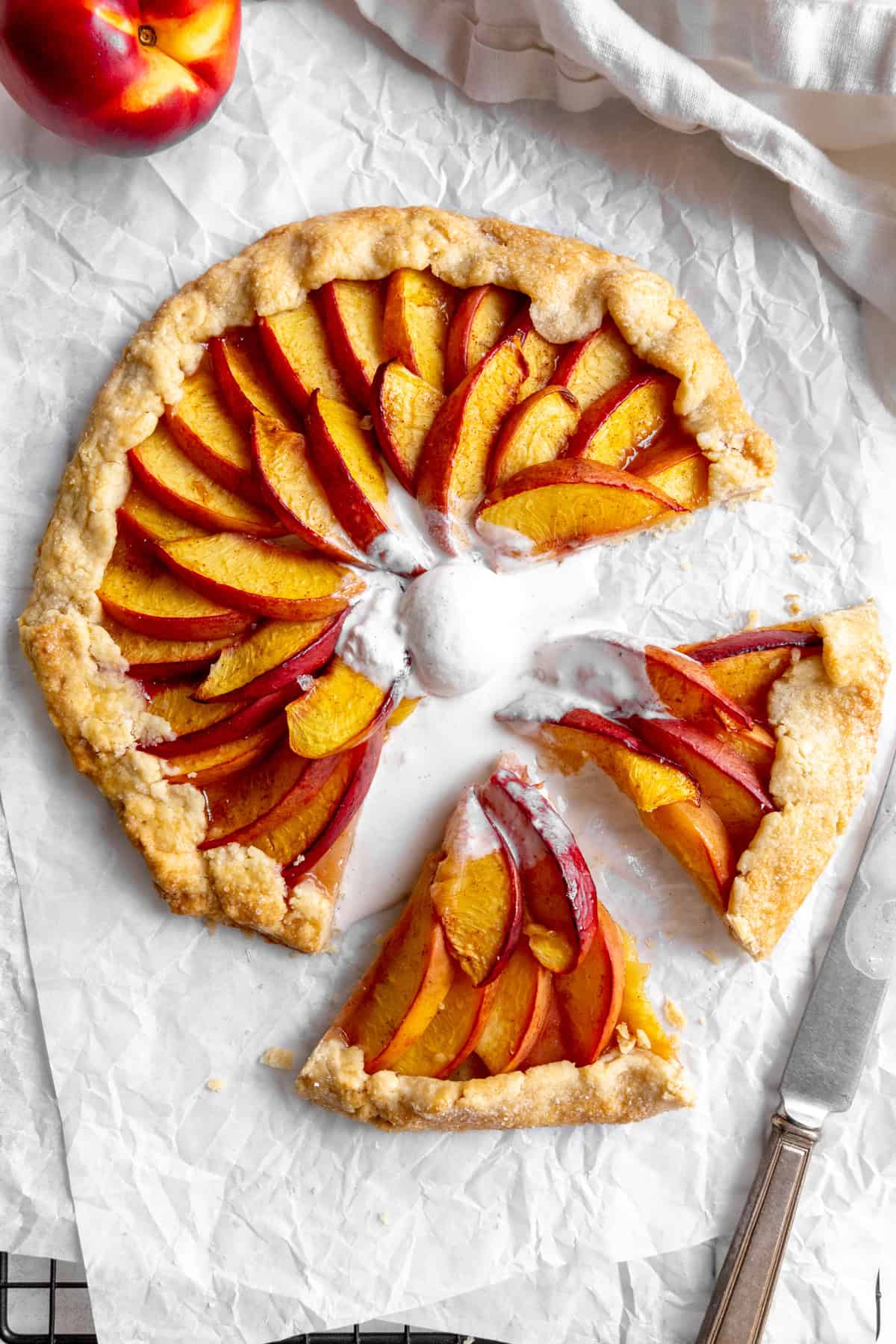 Sliced nectarine galette on parchment paper topped with melted vanilla ice cream.