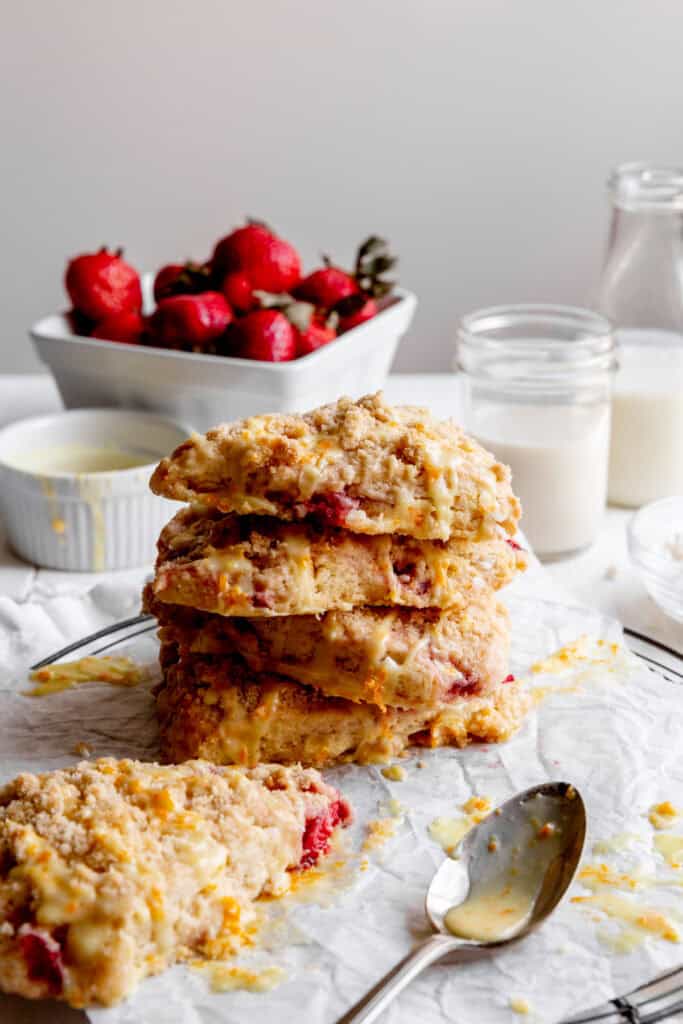 Stack of strawberry rhubarb scones, a jug of milk and a basket of strawberries.