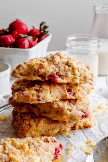 Stack of strawberry rhubarb scones, a jug of milk and a basket of fresh strawberries.
