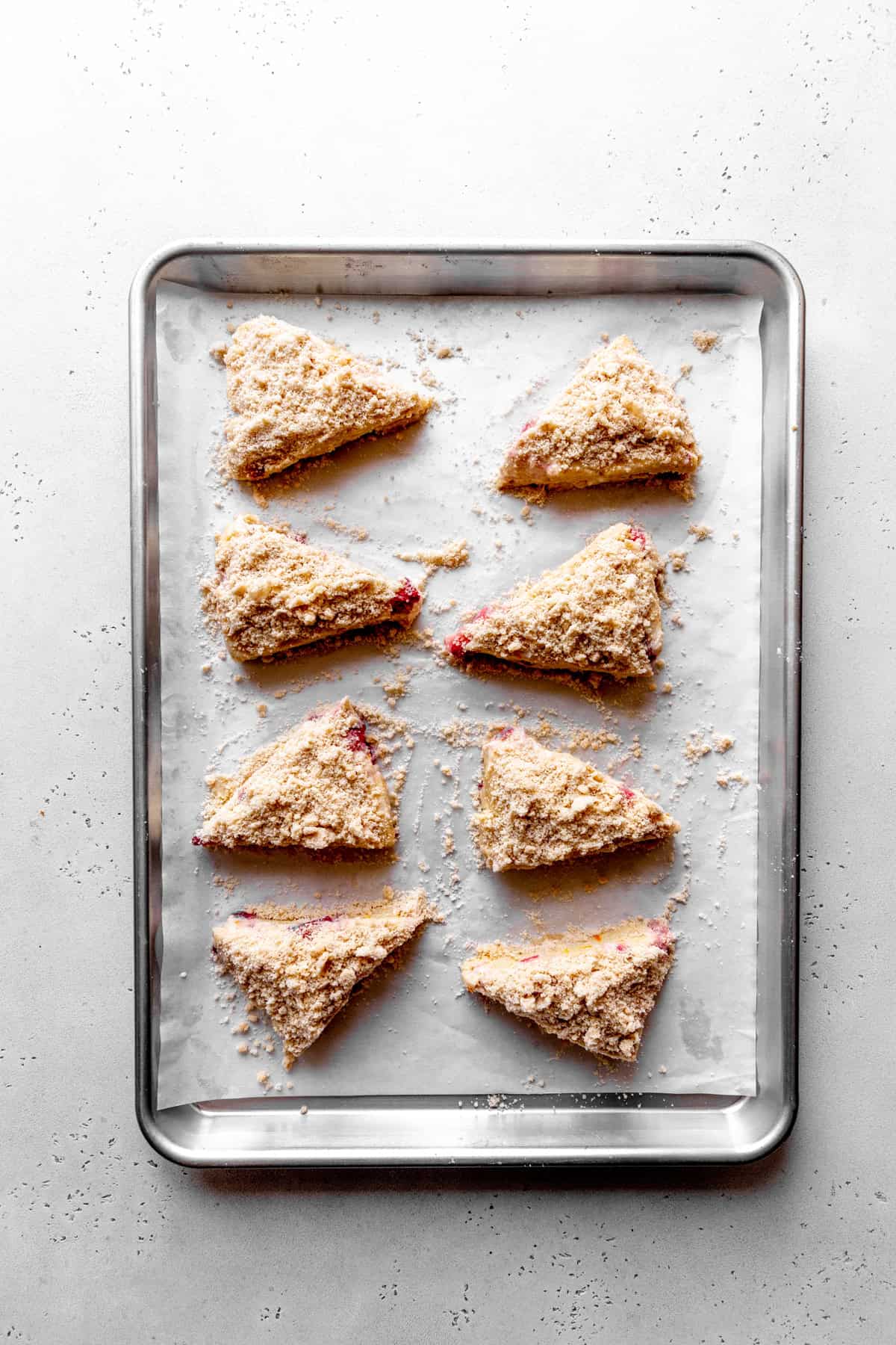 Unbaked strawberry rhubarb scones with streusel topping on a baking sheet.
