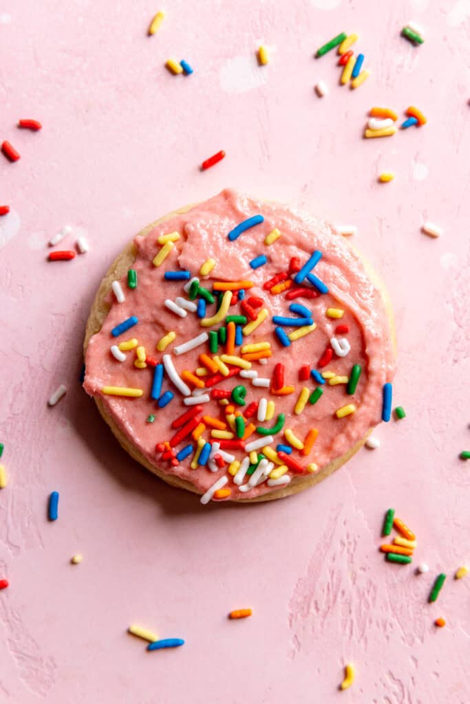 Sugar cookie on a pink surface covered in sprinkles.