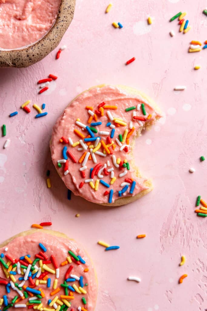 Sugar cookie with a bite taken out of it and a small bowl of frosting.