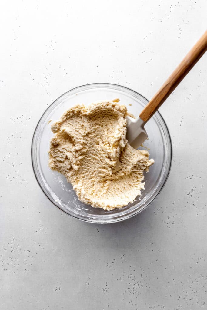 Sugar cookie dough in a glass bowl with a rubber spatula.