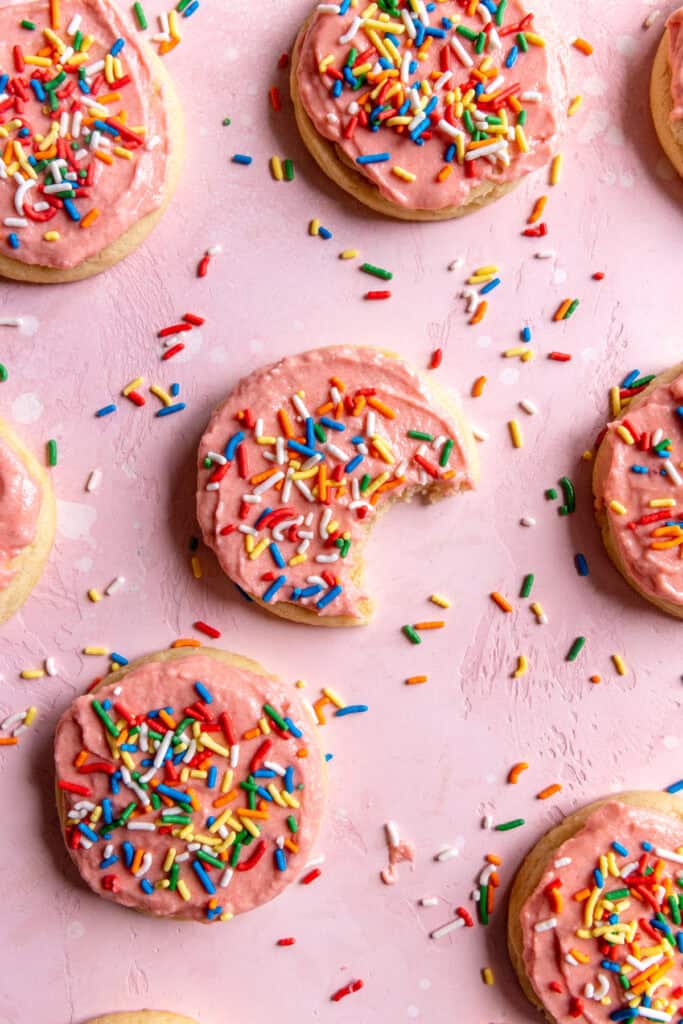 Sugar cookies spread out on a surface covered in sprinkles.