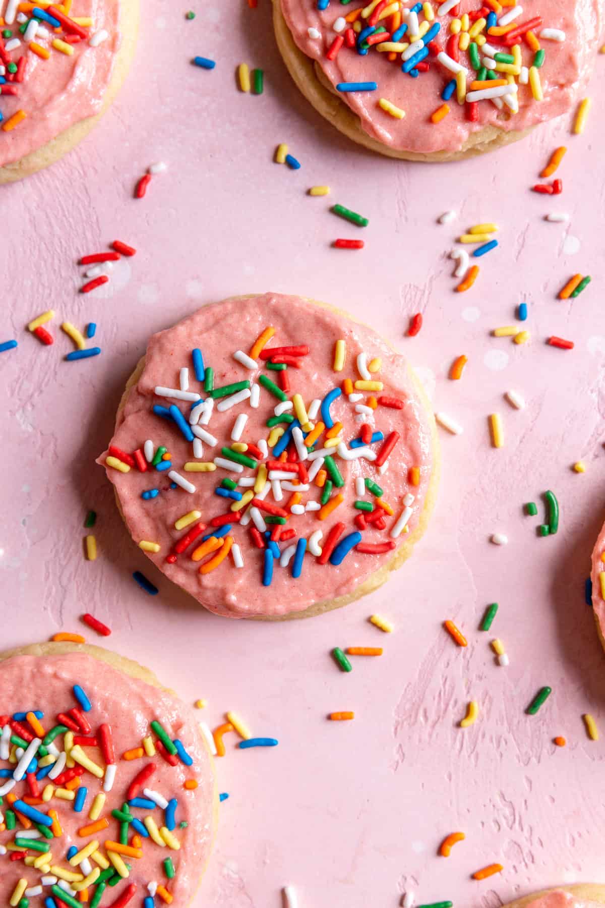 Sugar cookies spread out on a surface covered in sprinkles.