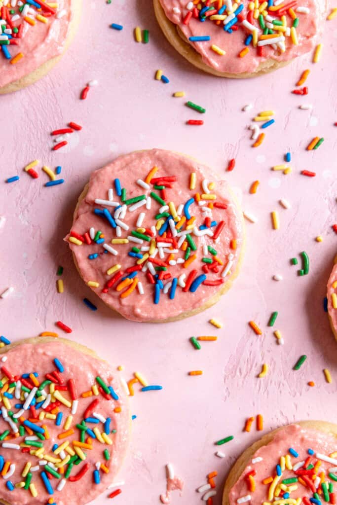 Sugar cookies spread out on a surface covered in sprinkles.