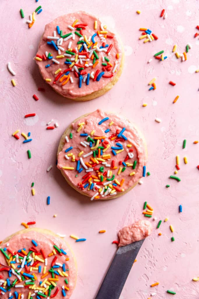 Sugar cookies on a pink background and a knife covered in strawberry frosting.