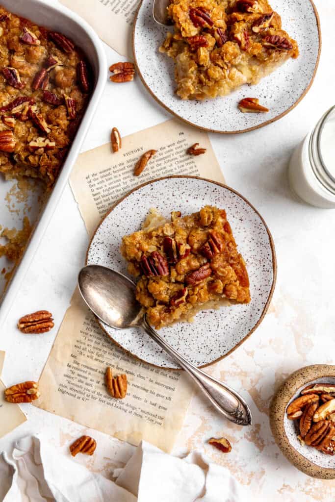 Banana cobbler on white plates with a cup of pecans and a glass of milk.