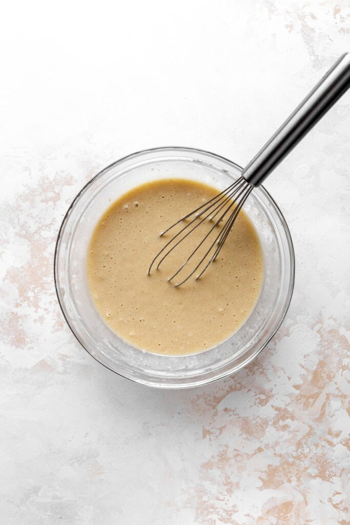 Glass bowl of cobbler batter and a wire whisk.