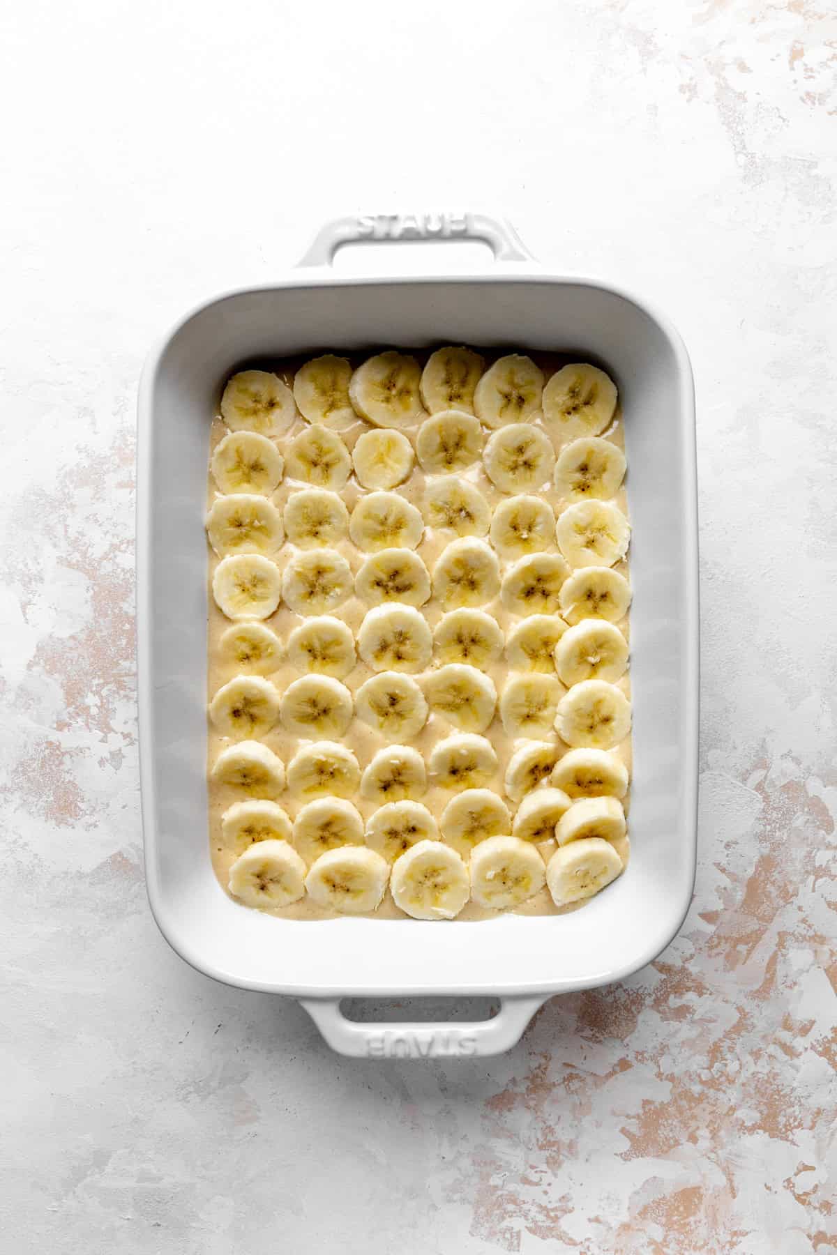Banana slices on cobbler batter in a white baking dish.