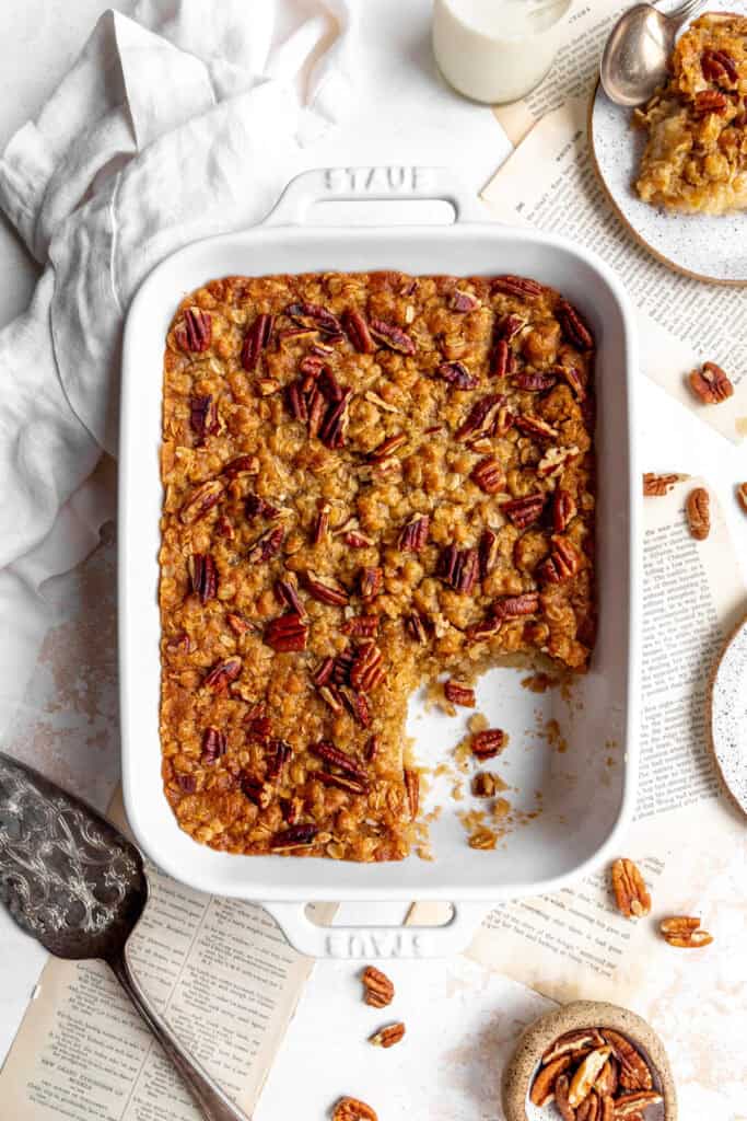 Banana cobbler topped with pecans, a linen napkin and a stack of plates.