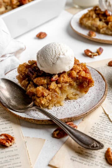 Banana cobbler topped with a scoop of vanilla ice cream on a plate with a spoon.