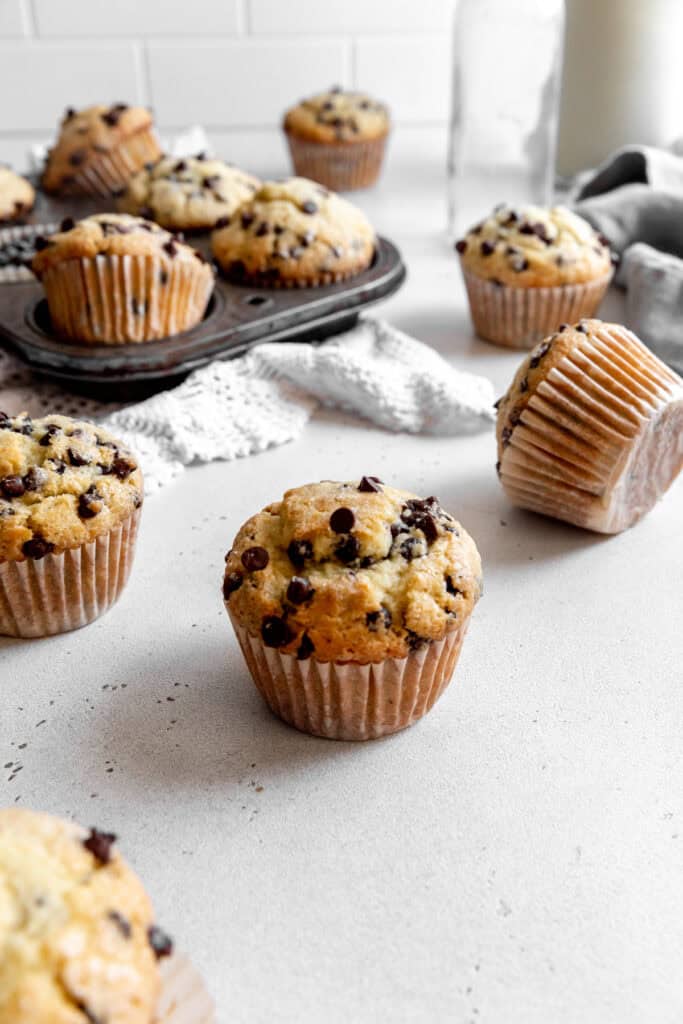 Chocolate chip muffins scattered across a counter and a jug of milk.
