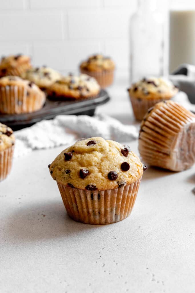 Chocolate chip muffin on a white counter in front of a pan of muffins.