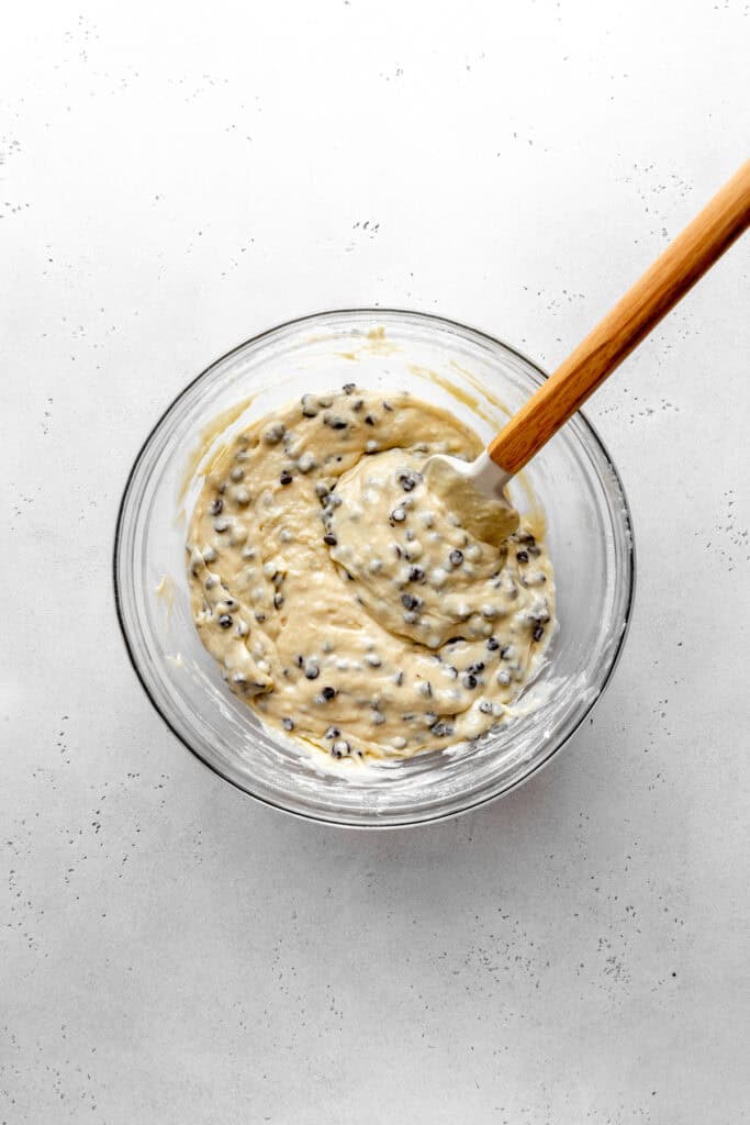 Glass bowl of chocolate chip muffin batter and a rubber spatula.