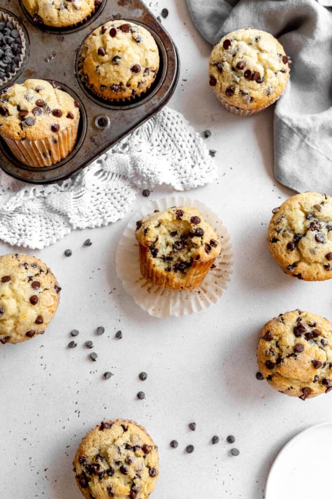 Chocolate chip muffin with a bite taken out of it surrounded by more muffins on a counter top.