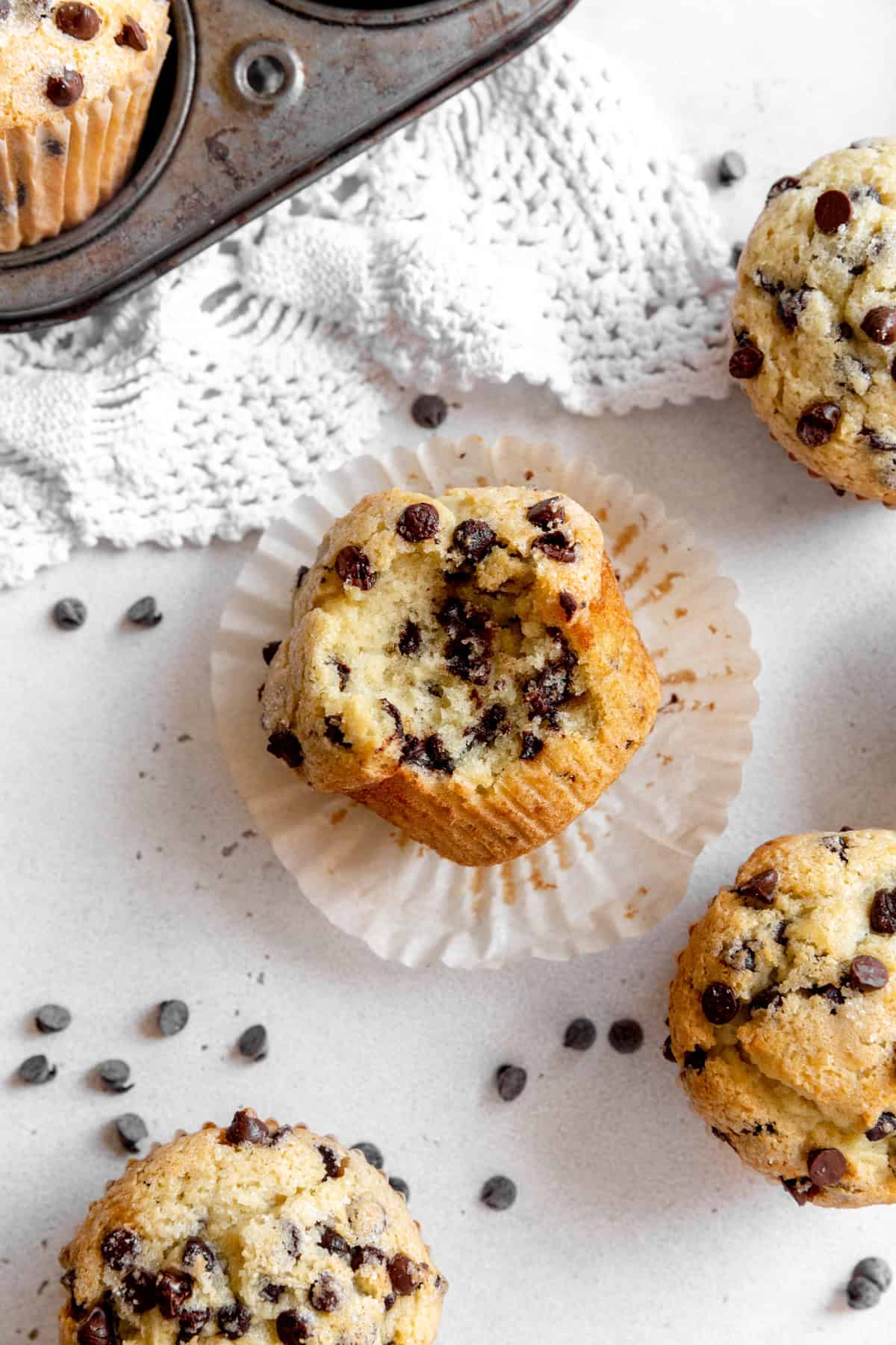 Chocolate chip muffin with a bite taken out of it sitting in its wrapper.