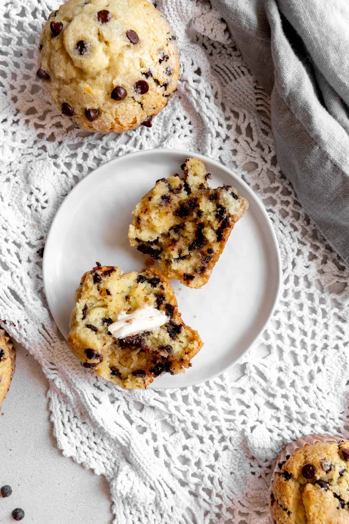 Chocolate chip muffin split in half on a plate, spread with butter.