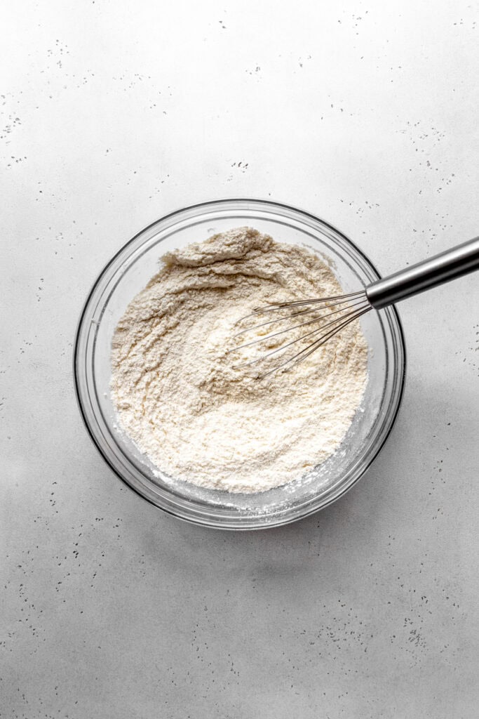 Glass bowl of flour and a wire whisk.