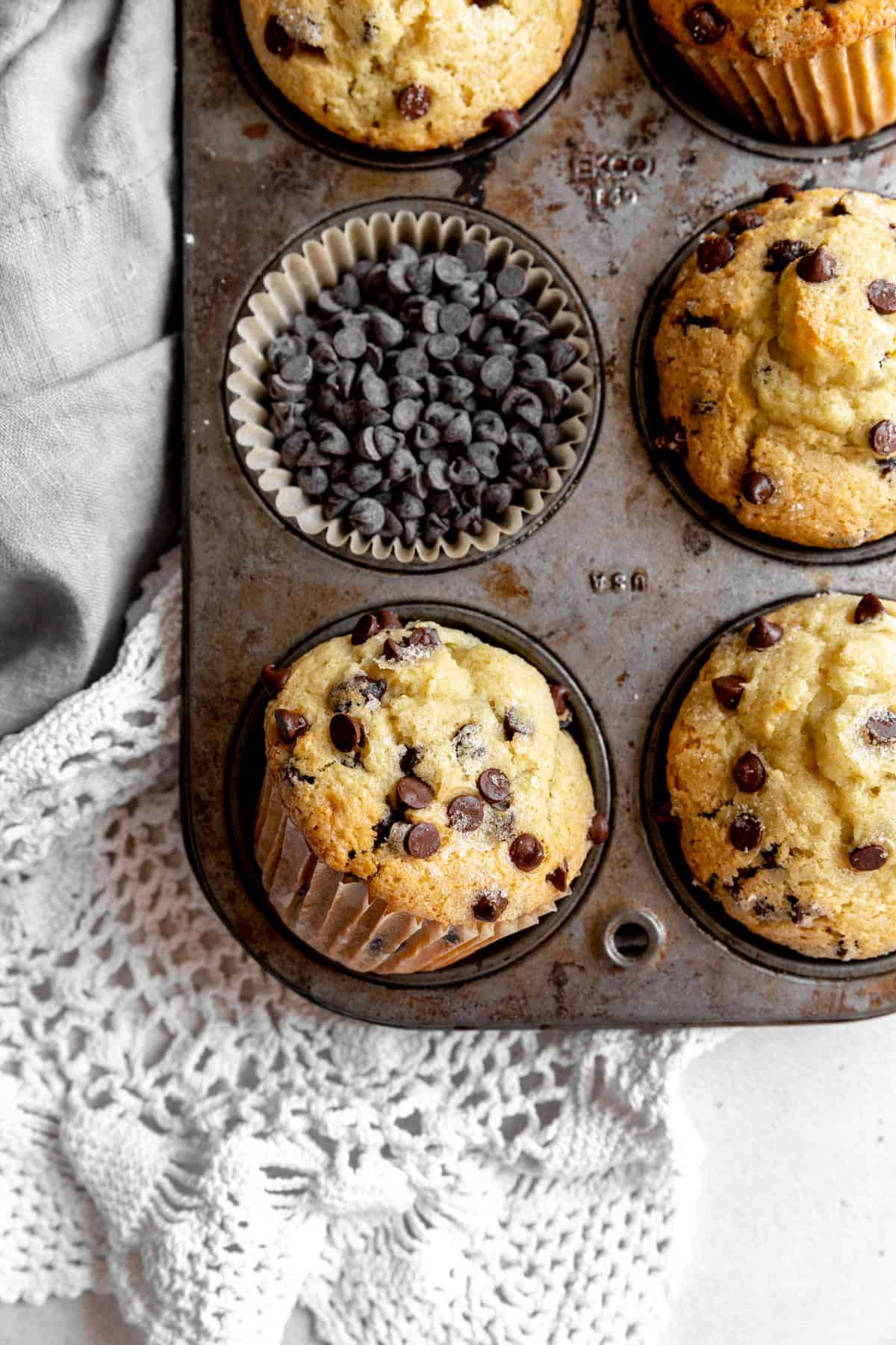 Chocolate chip muffins in a pan and a cup of chocolate chips.