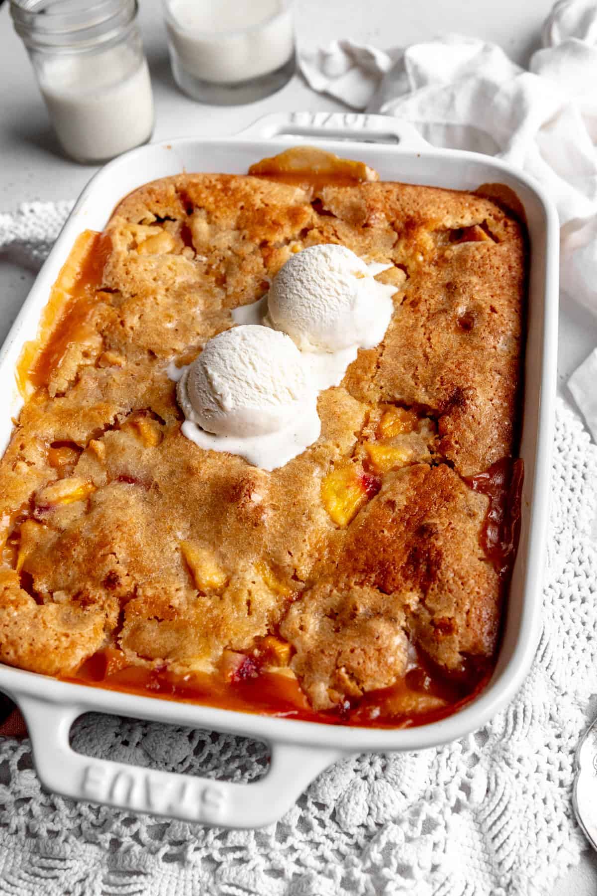 Peach cobbler topped with vanilla ice cream and two glasses of milk.