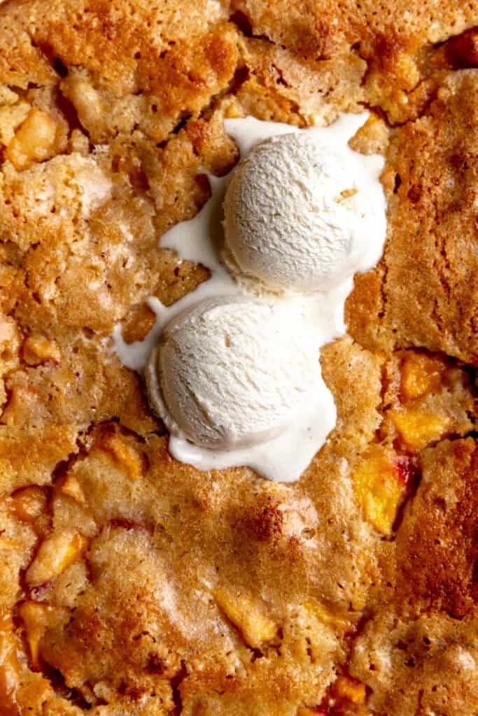 Peach cobbler topped with two scoops of vanilla ice cream.