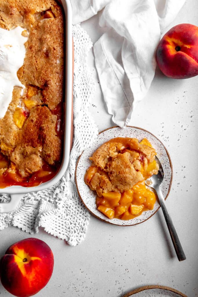 Peach cobbler on a plate and two whole peaches.