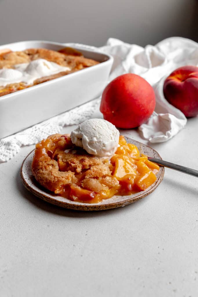 Peach cobbler on a plate topped with a scoop of vanilla ice cream.