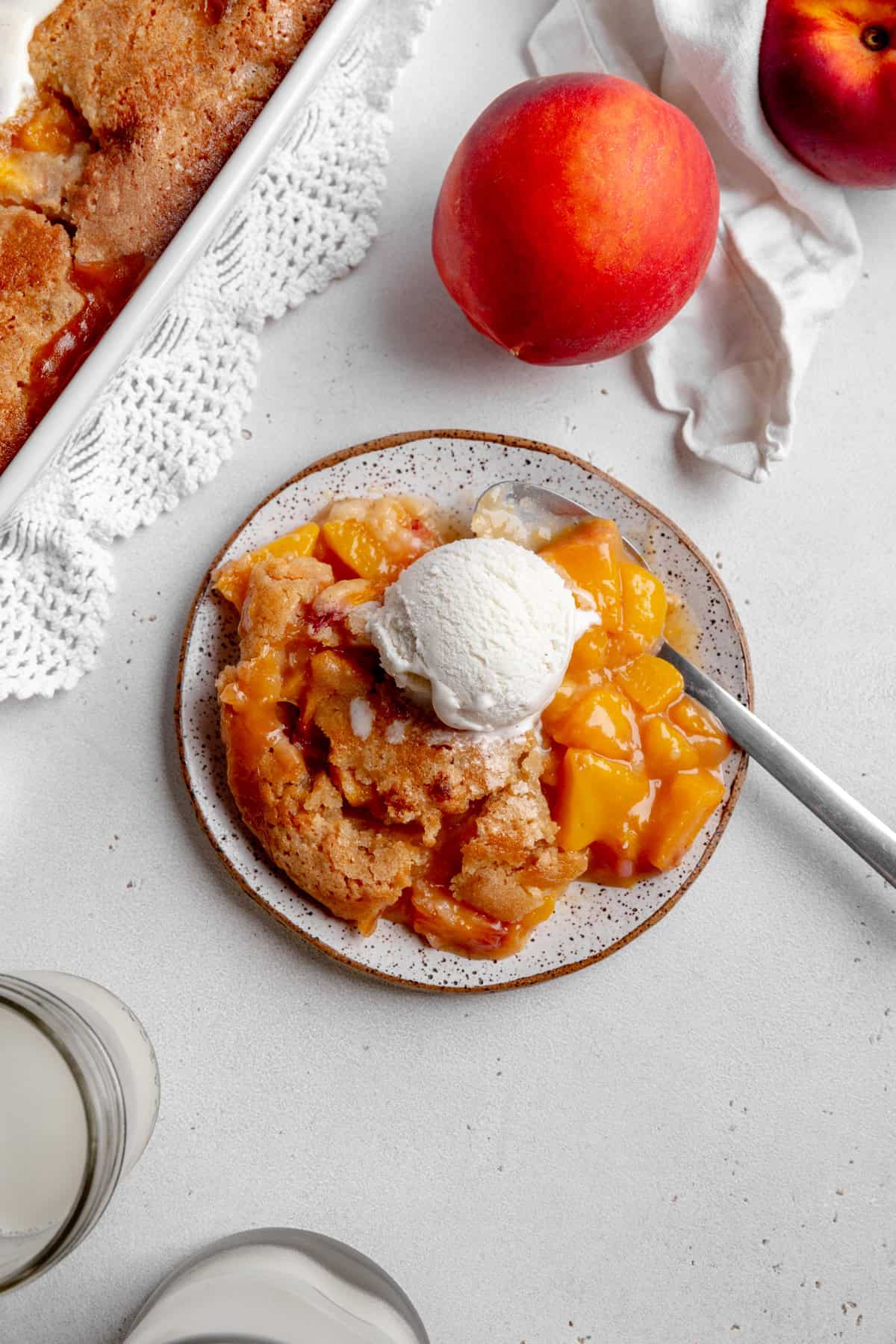 Peach cobbler on a plate topped with a scoop of vanilla ice cream and two whole peaches.