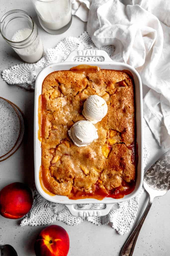 Peach cobbler topped with vanilla ice cream, fresh peaches and a glass of milk.